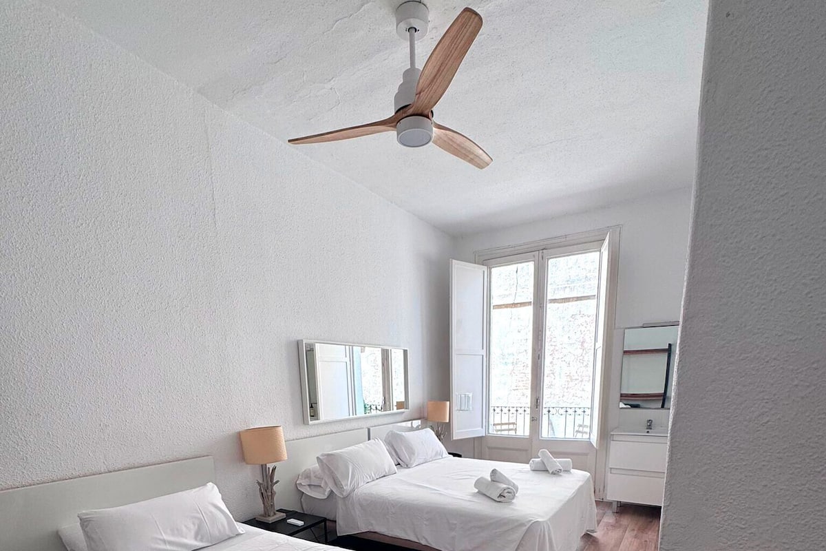 A hotel room with two beds, a ceiling fan, a large window, and a TV.