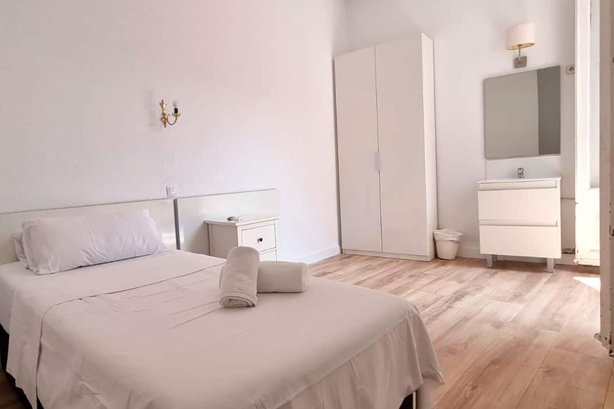 A bedroom with a bed, a nightstand, a wardrobe, and a bathroom with a mirror and sink.