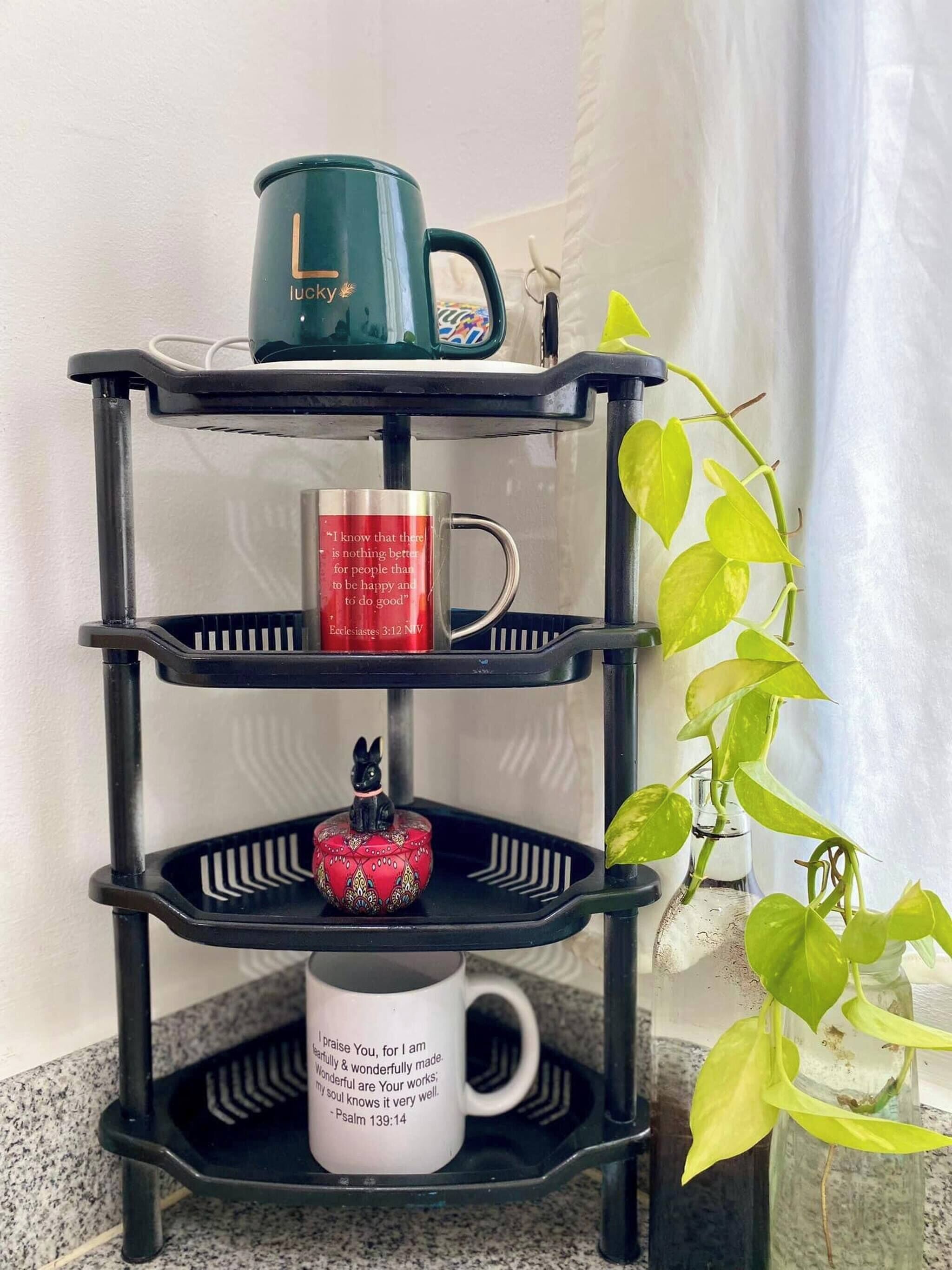 Estante preta de três níveis com diversos objetos, incluindo canecas e uma pequena estatueta.