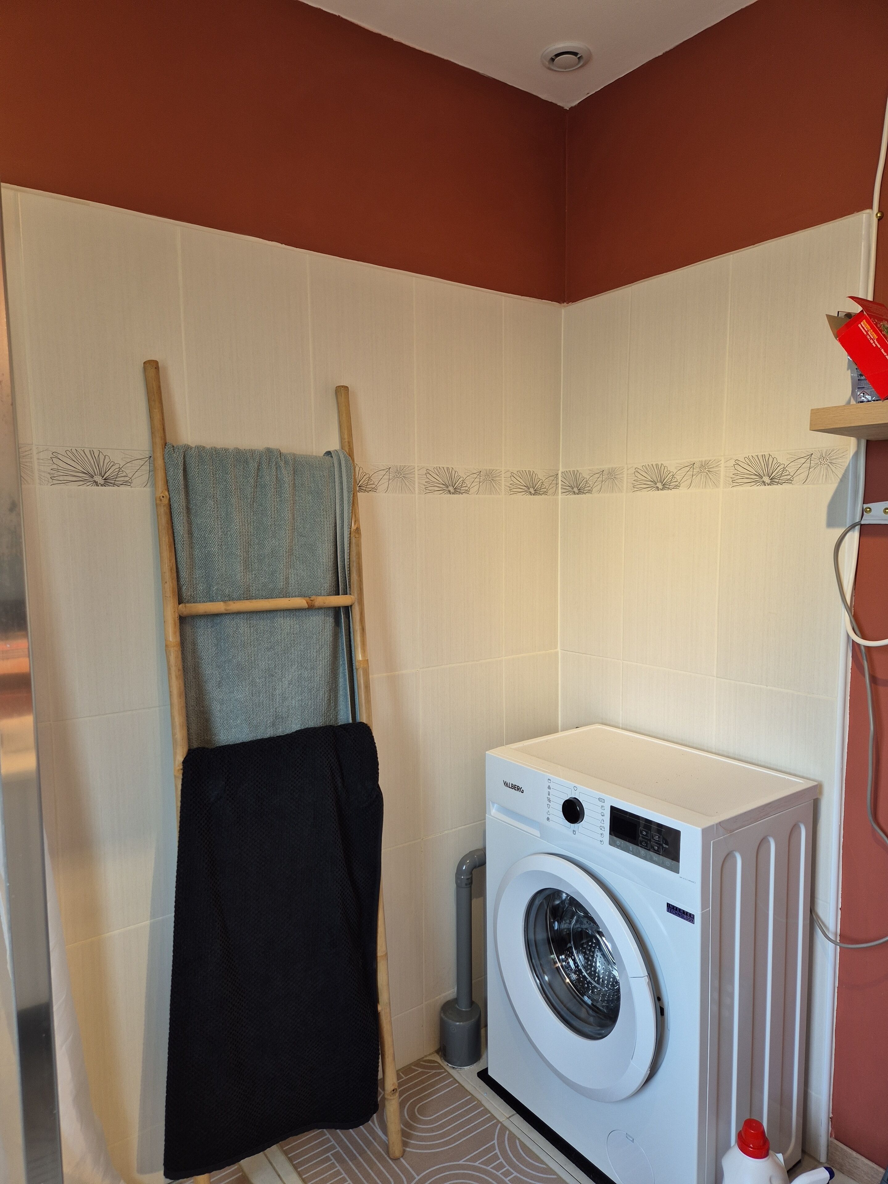 A laundry room with a washing machine, a drying rack, and a towel hanging on the wall.