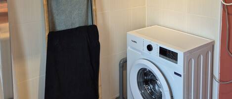A laundry room with a washing machine, a drying rack, and a towel hanging on the wall.