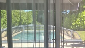 Visão através de cortinas translúcidas para uma área de piscina com terraço e espreguiçadeiras.