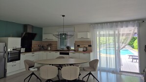 Cozinha moderna com armários brancos, forno embutido e área de refeições com mesa redonda e cadeiras.