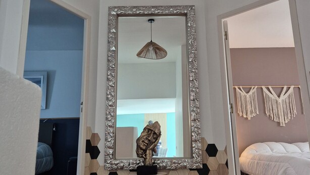 Quarto moderno com um espelho grande, uma luminária pendente suspensa, um painel de parede em macramé e um papel de parede com padrão geométrico.