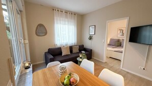 Una sala de estar moderna con una mesa de comedor de madera, un sofá de color oscuro y un televisor montado en la pared.