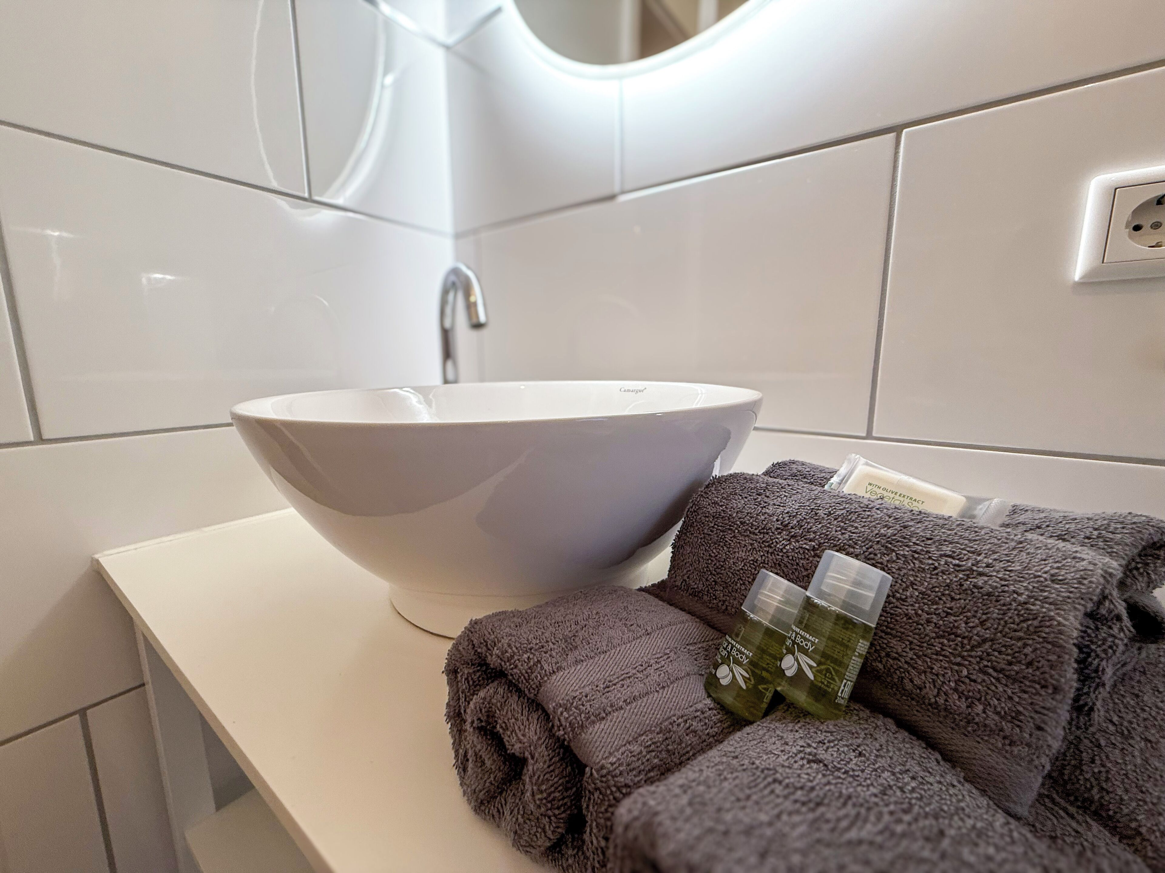 Een badkamer met een witte wastafel, een spiegel en een handdoekhouder met handdoeken en flesjes.