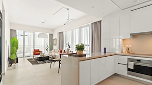 A modern kitchen with white cabinets, a central island, and a dining area with a sofa and table. - Silkhaus Canal Front 9 A tower (Dubai)