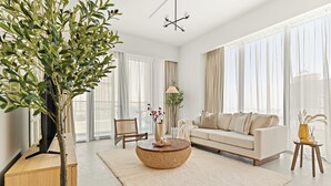 A modern living room with a large window, a sofa, a coffee table, and a plant. - Silkhaus Canal Front 9 A tower (Dubai)