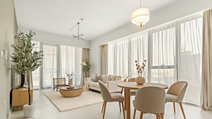 A modern living room with a sofa, dining table, chairs, and a large window with curtains. - Silkhaus Canal Front 9 A tower (Dubai)