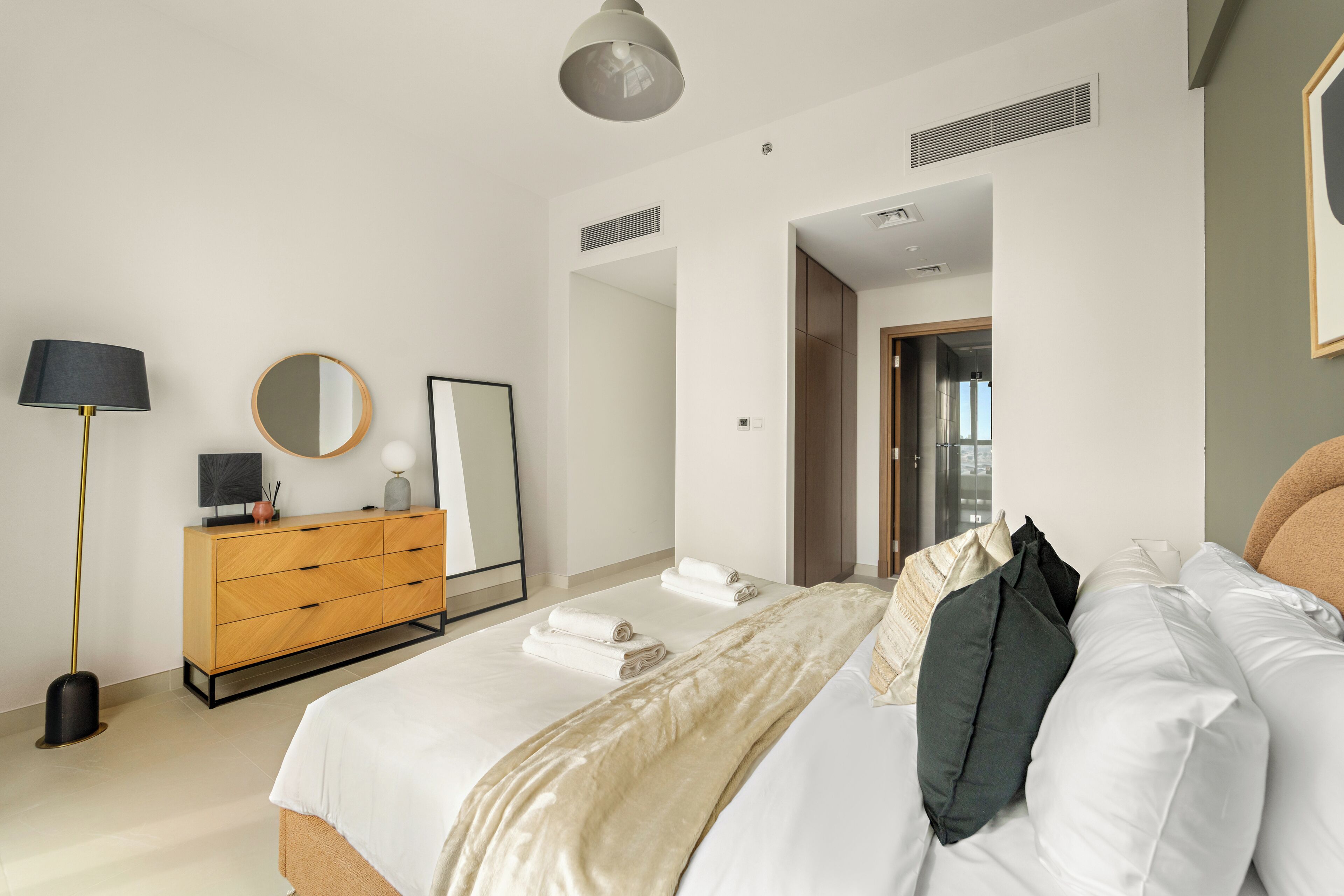 A modern bedroom with a bed, bedside table, lamp, mirror, and wardrobe.