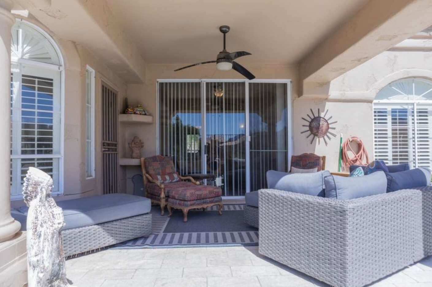 Une terrasse couverte, aménagée avec des meubles en osier, un ventilateur de plafond et un élément décoratif mural en forme de soleil rayonnant.