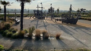 Un parque costero con exhibición de naufragio, bancos y palmeras.
