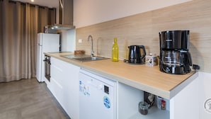 Una cocina compacta con un lavamanos, una cafetera, un hervidor y un lavavajillas.