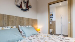 Un dormitorio con cabecera de madera, cama con ropa de cama floral, mesita de noche con lámpara y decoración náutica de un velero colgado en la pared.