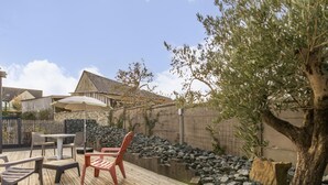 Una terraza de madera con mobiliario exterior, un muro de piedra y un árbol.