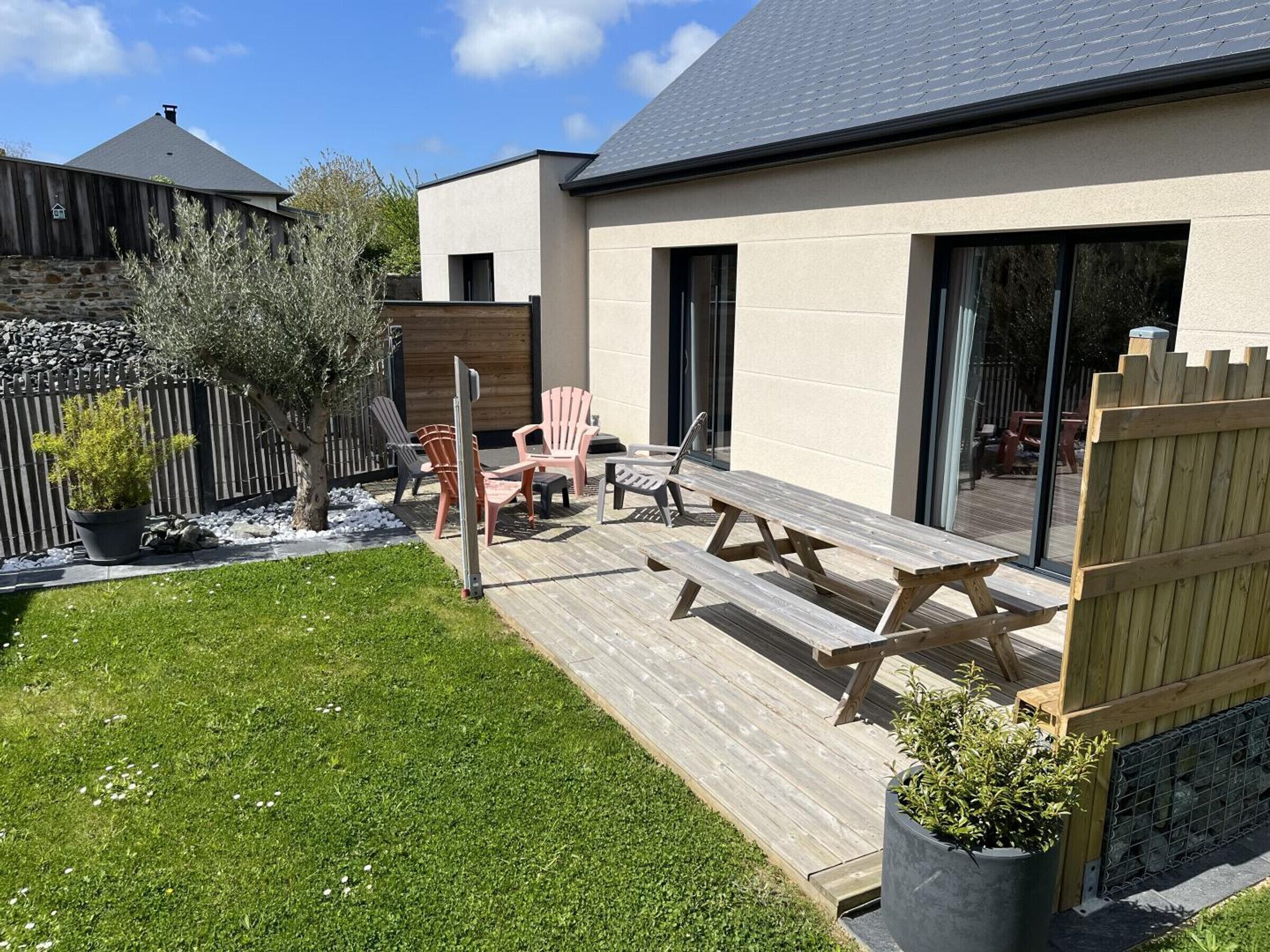 A modern house with a wooden deck, outdoor seating, and a fenced backyard.