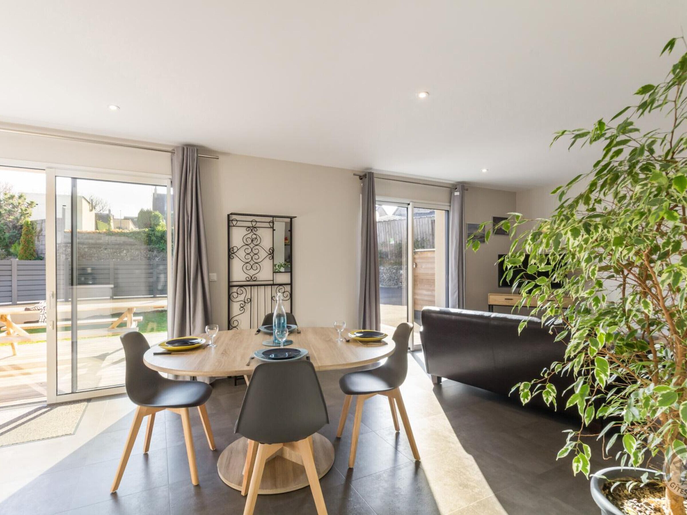 Uma área de jantar moderna com mesa de madeira, cadeiras pretas e uma porta de correr de vidro que dá para um pátio externo.