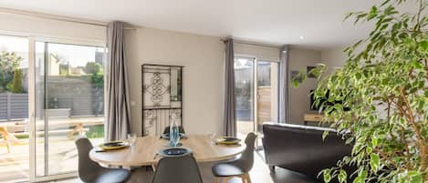 Uma área de jantar moderna com mesa de madeira, cadeiras pretas e uma porta de correr de vidro que dá para um pátio externo.