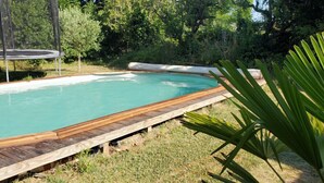 Ein Schwimmbecken mit Holzterrasse, umgeben von Gras und Bäumen.