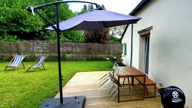 Eine Holzterrasse mit Tisch, Stühlen, einem Grill und einem Sonnenschirm.