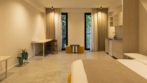 Une chambre d’hôtel moderne, dotée d’un grand lit, d’un bureau, d’une petite table ronde et offrant une vue sur la verdure par les fenêtres.