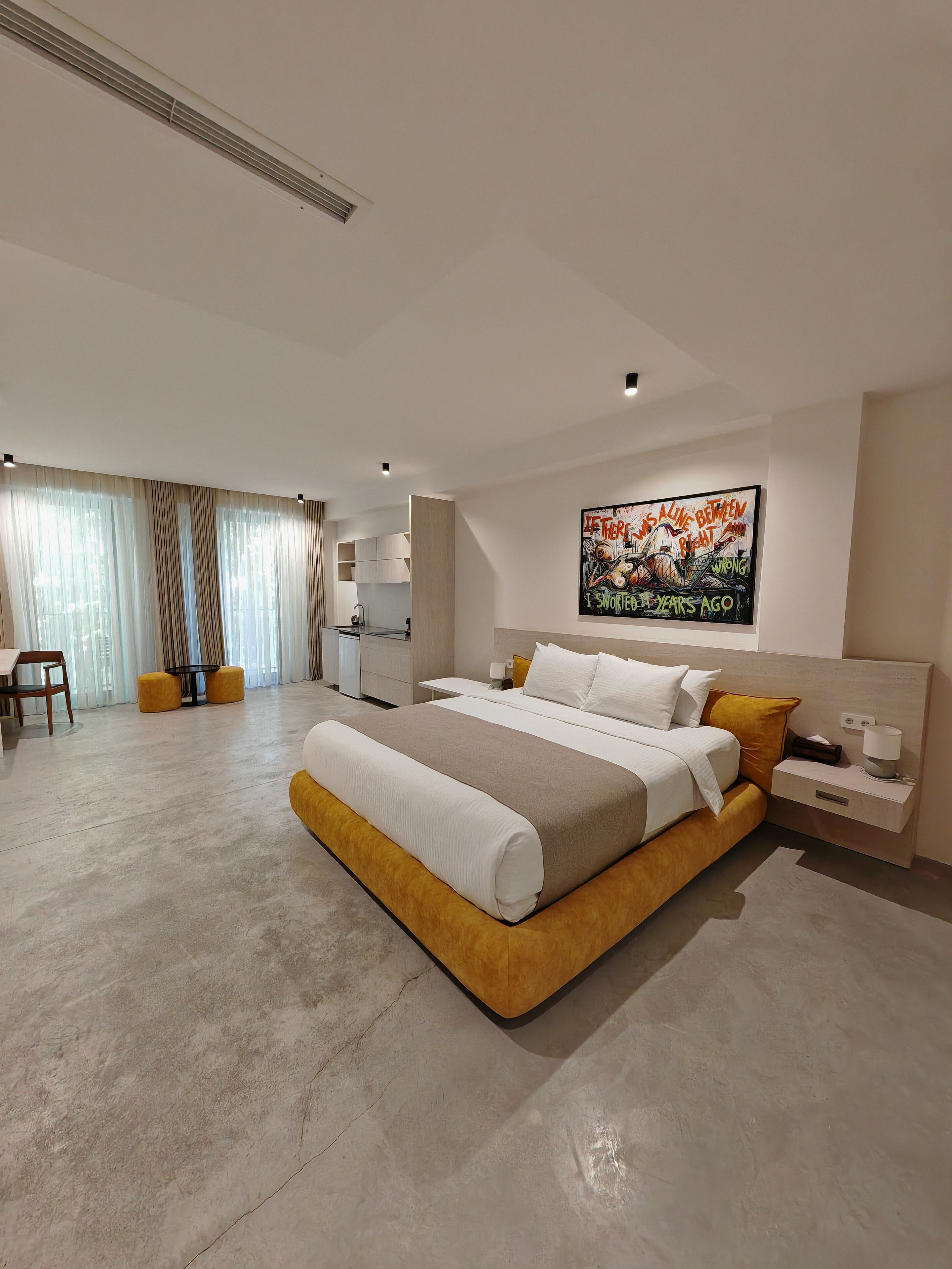 A modern bedroom with a large bed, bedside tables, a nightstand, and a wall-mounted artwork.