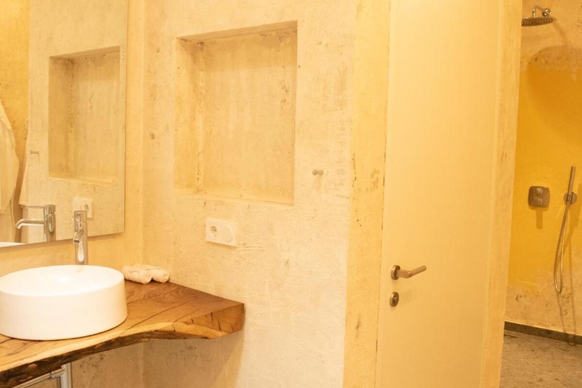 A bathroom with a wooden vanity, a white sink, a mirror, and a shower area.