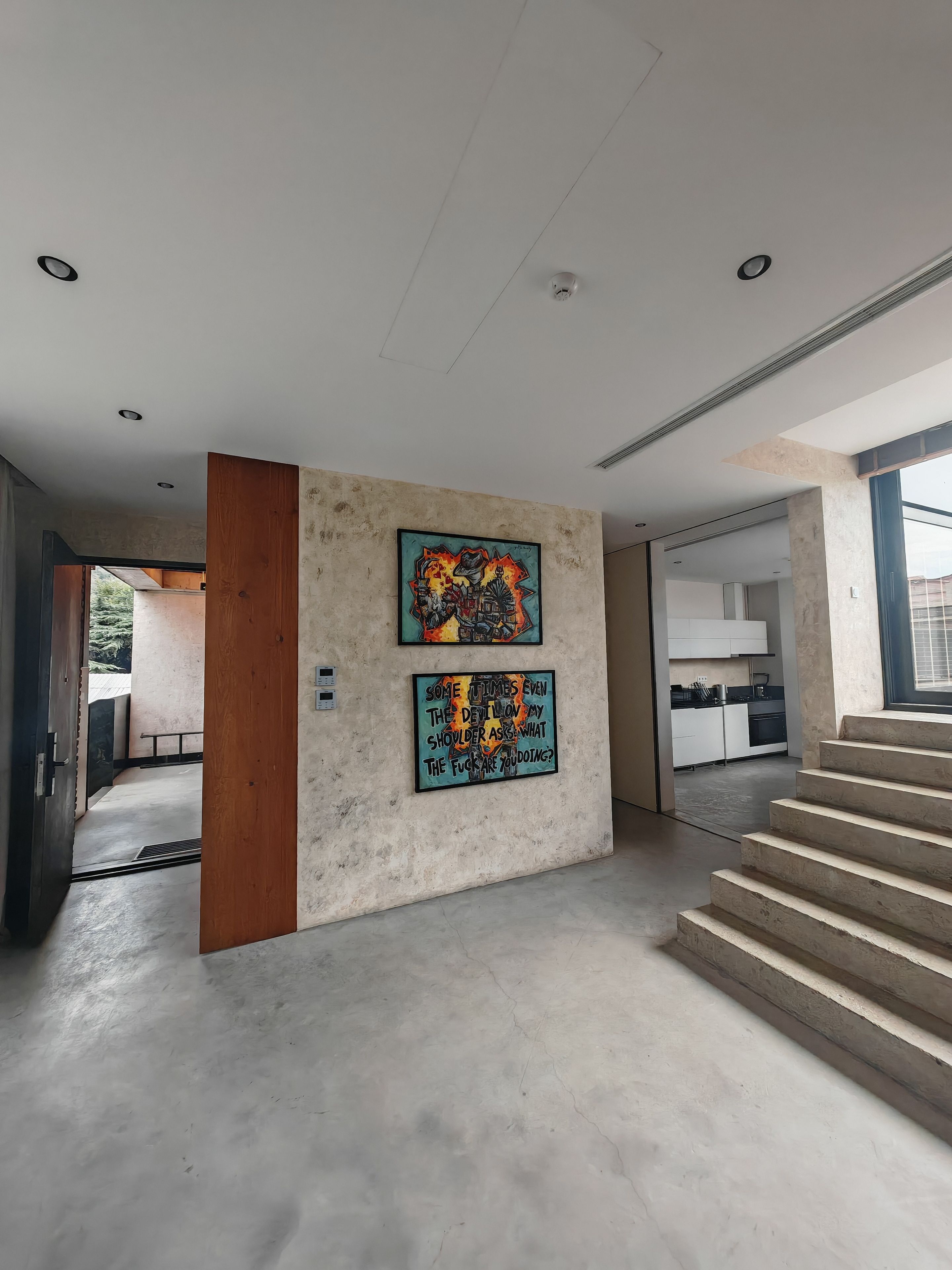 Un interior moderno con una escalera, dos obras de arte en la pared y una cocina visible a través de un pasillo abierto.