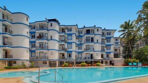 Un hotel con varios balcones, piscina y terraza con mobiliario exterior.