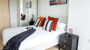 A modern bedroom with a large bed, a bedside table, a mirror, and a colorful abstract painting on the wall.