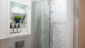 A modern bathroom with a glass shower enclosure, a geometric tile backsplash, and a shelf with toiletries.