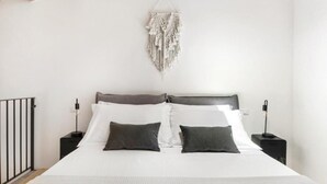 Et soveværelse med en seng, to sengeborde med lamper, et macramé-ophæng på væggen og et træloft.