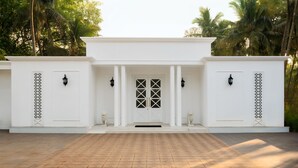 Un bâtiment blanc avec une porte centrale, flanqué de deux colonnes et de deux statues.