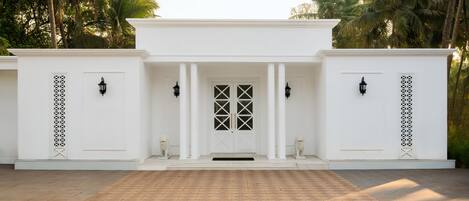 A white building with a central door, flanked by two columns and two statues.