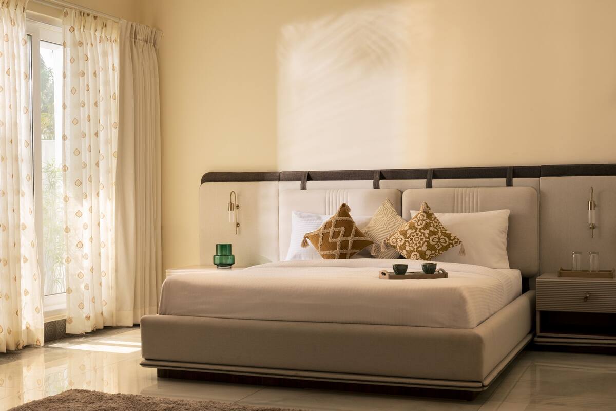 A bedroom with a large bed, a nightstand, a bedside table, and a window with curtains.
