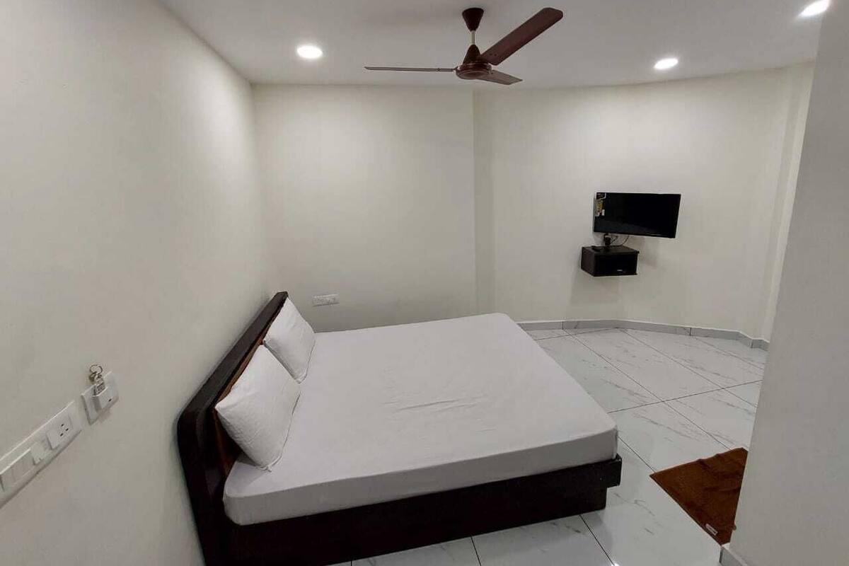 Ein Schlafzimmer mit einem Bett, einem Deckenventilator, einem an der Wand montierten Fernseher und einem Fliesenboden.