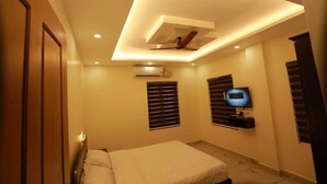 A bedroom with a bed, ceiling fan, air conditioning unit, TV, and window blinds. - Aman Residency (Thodupuzha)