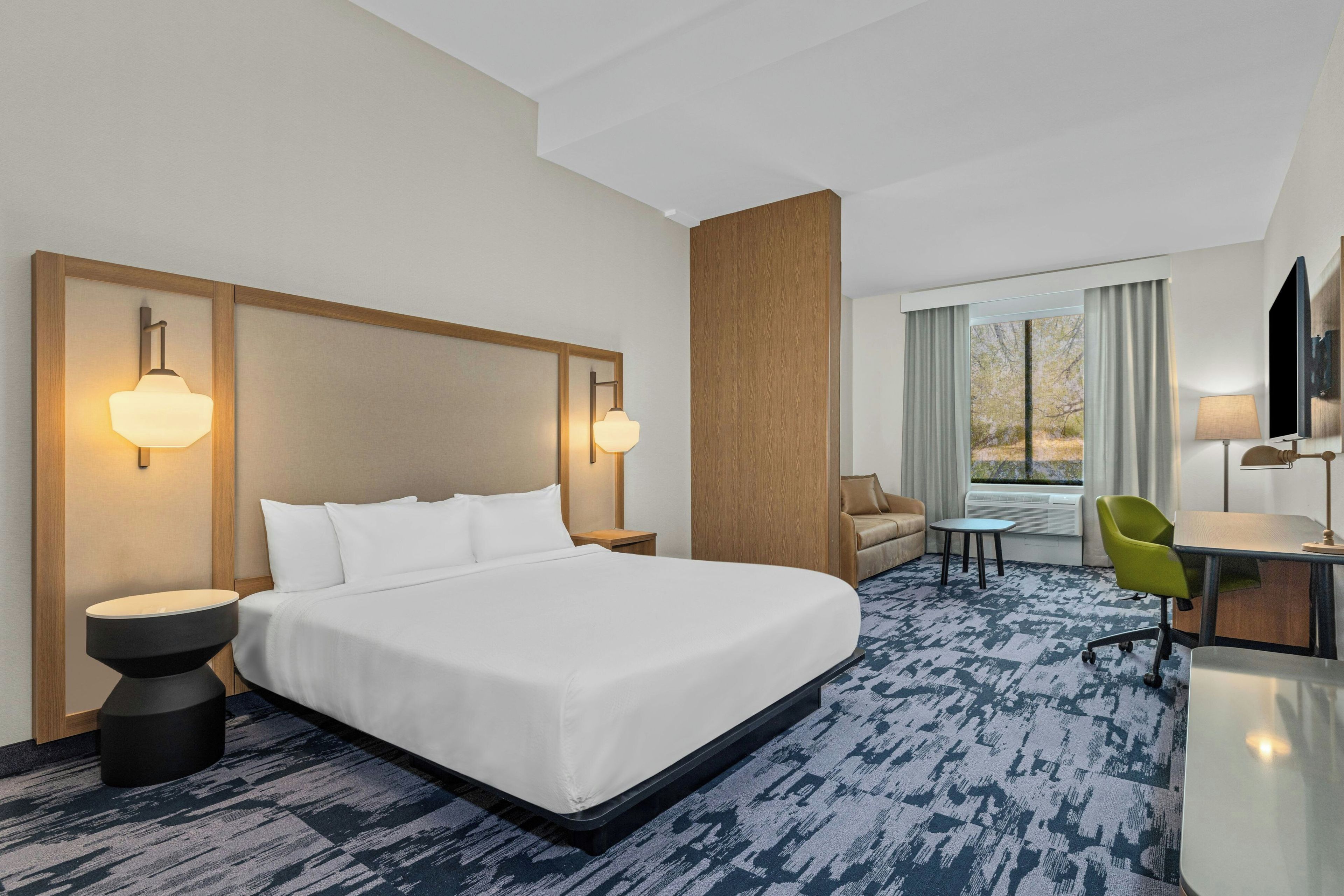 Habitación de hotel con una cama grande, dos mesitas de noche, un escritorio, una silla, un televisor y una ventana con cortinas.