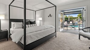 A four-poster bed with a white and black color scheme, a nightstand, a lamp, and a view of an outdoor pool area.