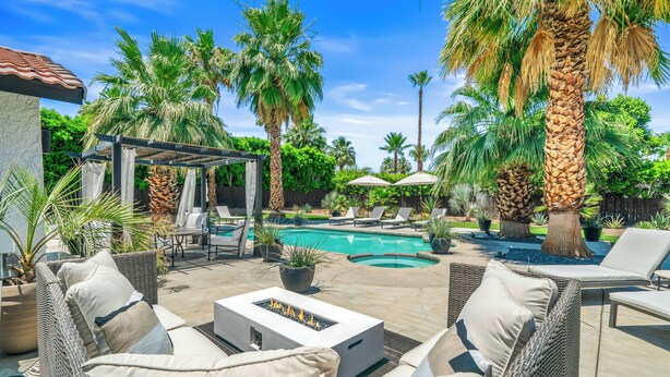 A poolside area with wicker furniture, a fire feature, and palm trees.