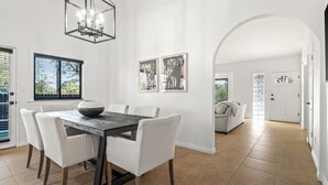 A dining area with a dark wooden table and white chairs, a chandelier, and two framed artworks on the wall.