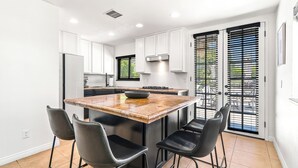 A modern kitchen with white cabinets, a central island with stools, and a sliding glass door leading to a patio.