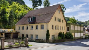 Ein zweistöckiges Gebäude mit einem geneigten Dach, zahlreichen Fenstern und einem umzäunten Garten.