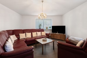 A living room with a sectional sofa, a coffee table, a television, and a wooden cabinet. - Apartment 'Ferienwohnung in Bad Berneck' with Shared Terrace and Wi-Fi (Bad Berneck im Fichtelgebirge)