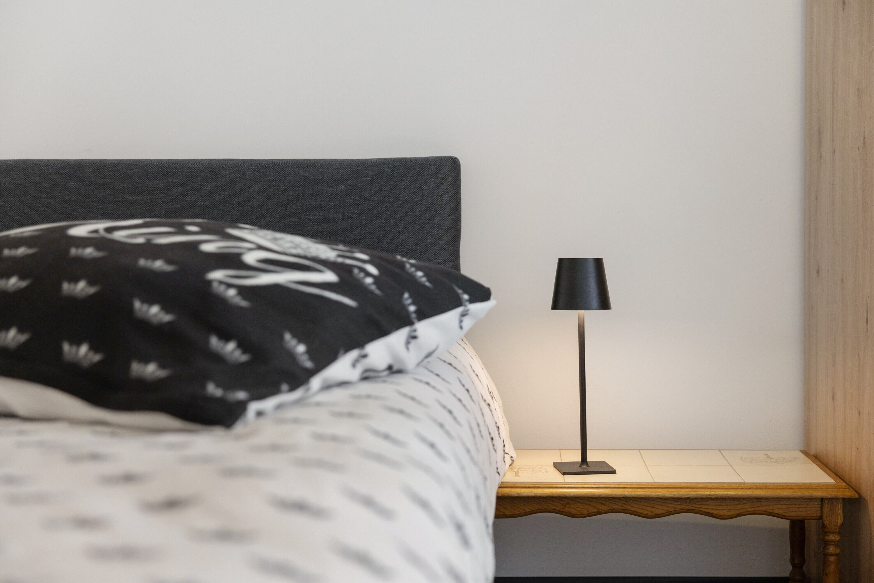 A bed with a patterned pillow, a bedside lamp, and a wooden nightstand.