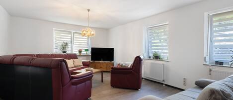 A living room with a red sofa, a beige sofa, a wooden coffee table, and a TV.