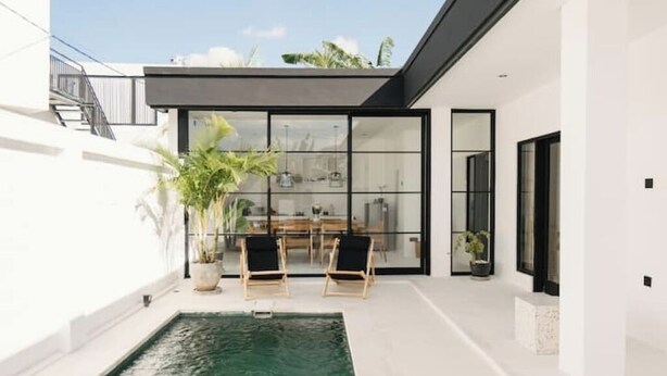 Una casa moderna con piscina, puertas de vidrio y un comedor con sillas.