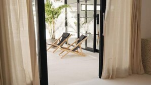 Una habitación con un ventanal grande, dos sillones y vistas a palmeras afuera.
