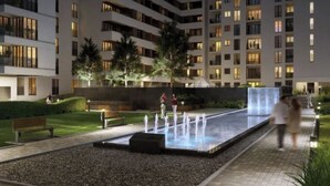 Une cour d’hôtel moderne agrémentée d’un élément aquatique, de bancs et de palmiers.