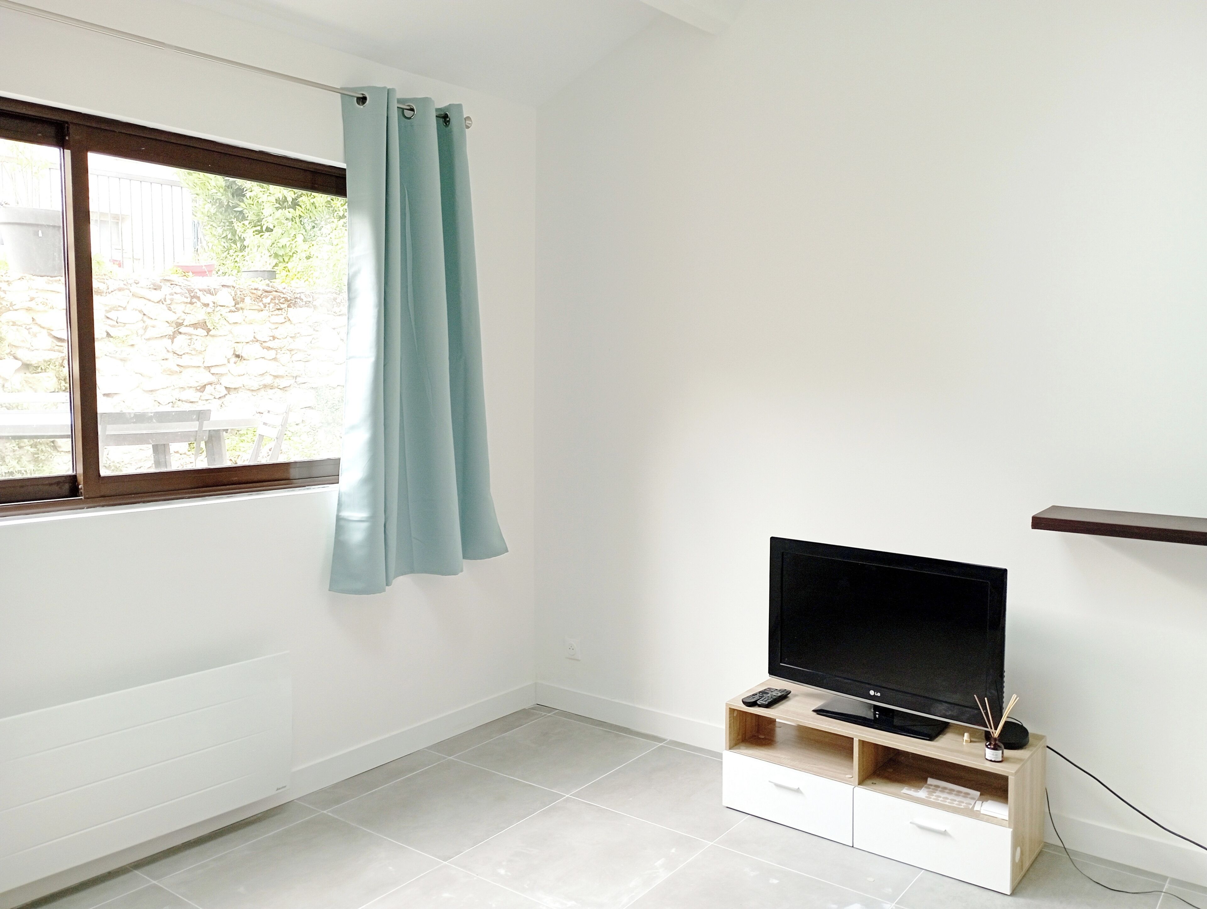A room with a window, a TV on a wooden stand, and a curtain.